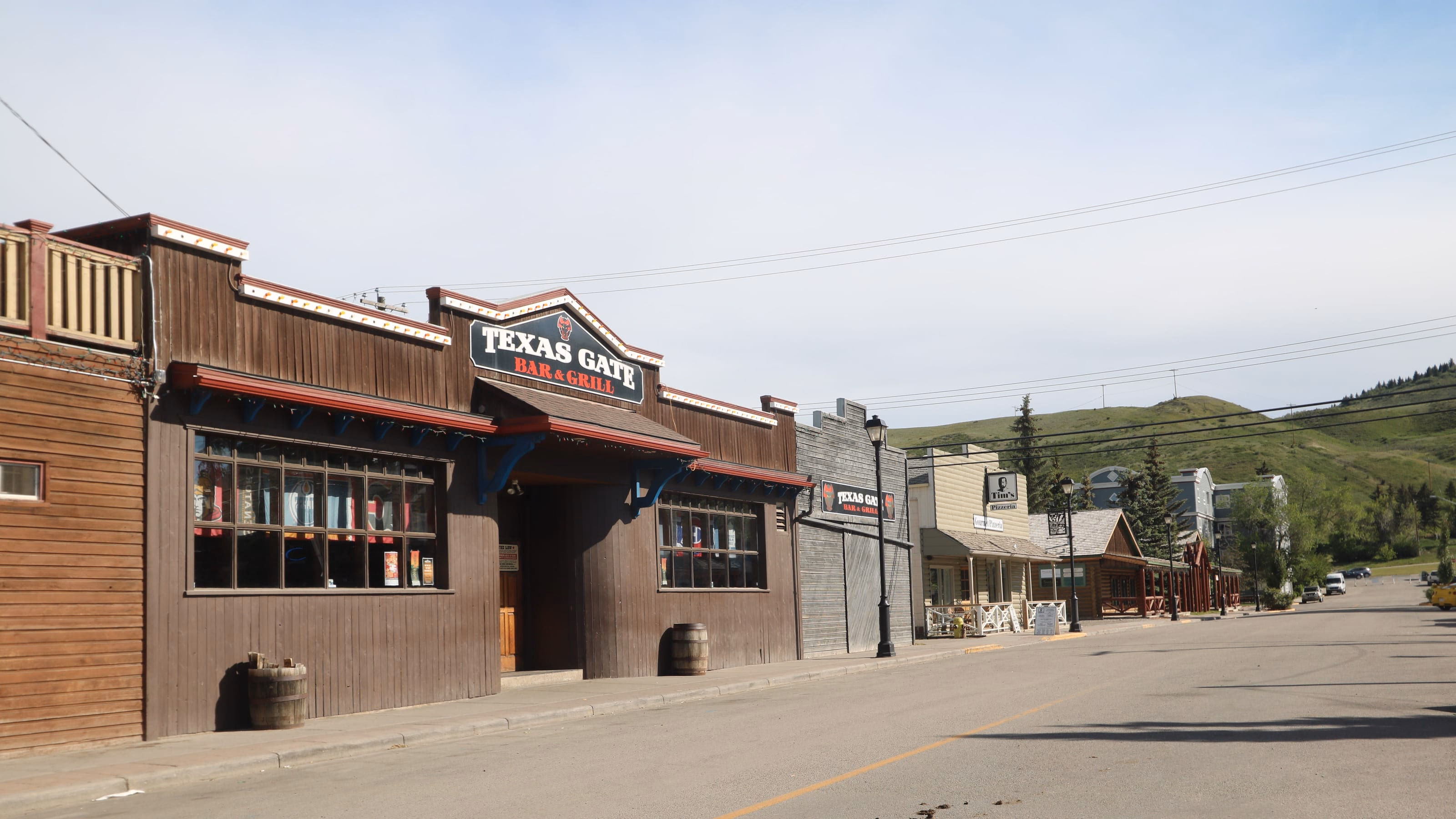 Western-style wooden storefronts along Main Street in historic downtown Cochrane, Alberta, with green hills behind