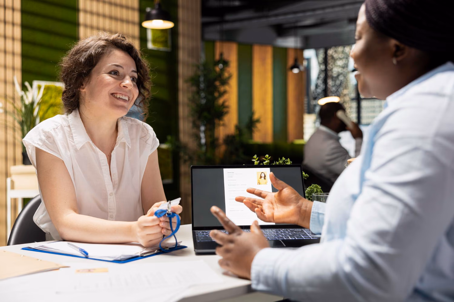 A service business professional smiling while meeting a client at a desk with a laptop