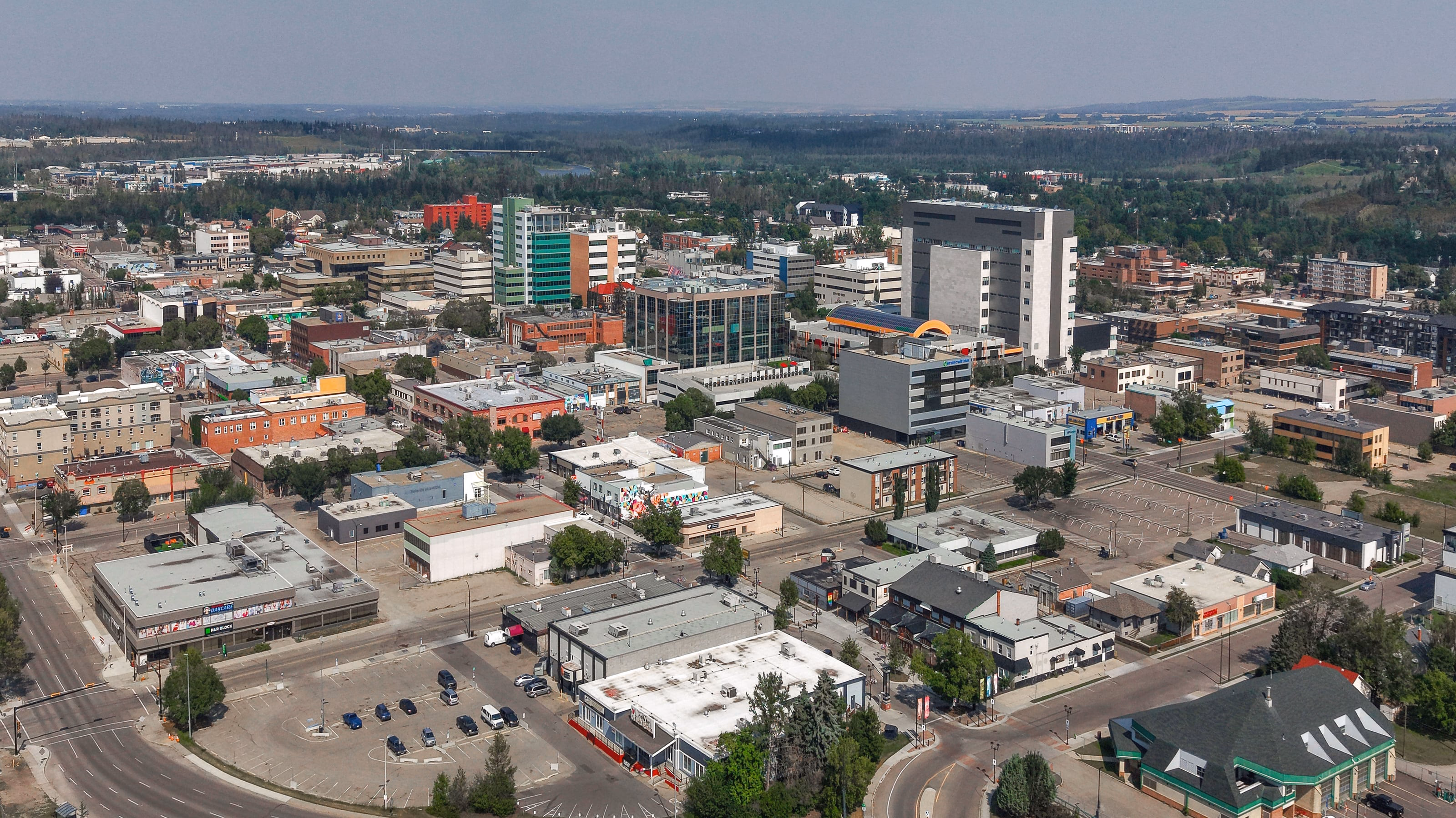 Aerial view of downtown Red Deer, Alberta, in summer, with office towers, low-rise streets and the tree-lined river valley beyond