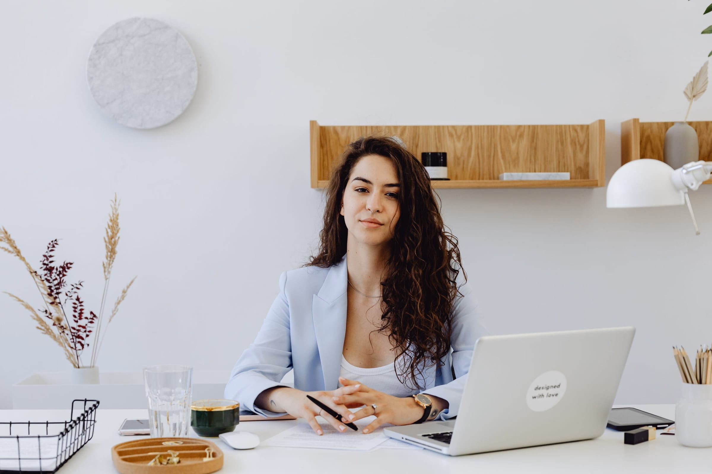 A business owner in a light blazer sitting at a bright, minimal office desk with a laptop and paperwork